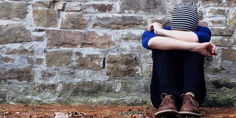 A young person sitting alone against a stone wall